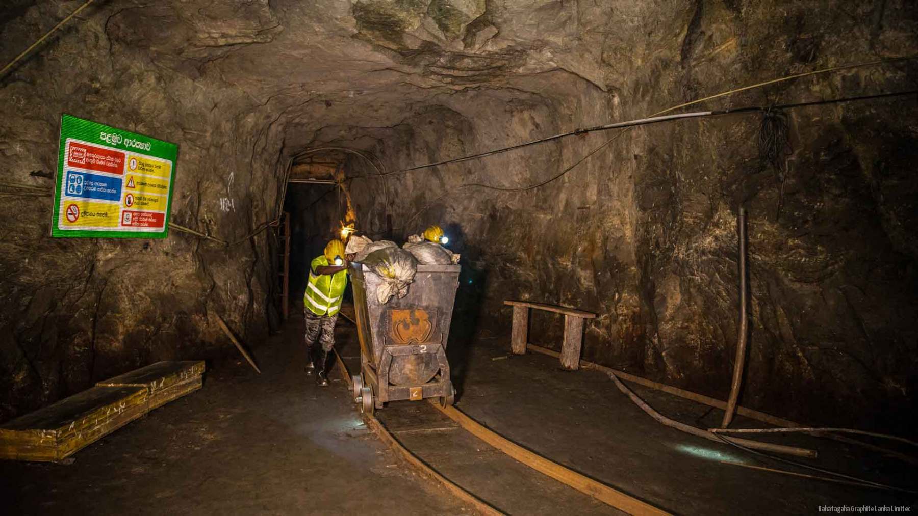 An underground haulage level in the Kahatagaha mine, with a miner moving a loaded ore tub along the rails.