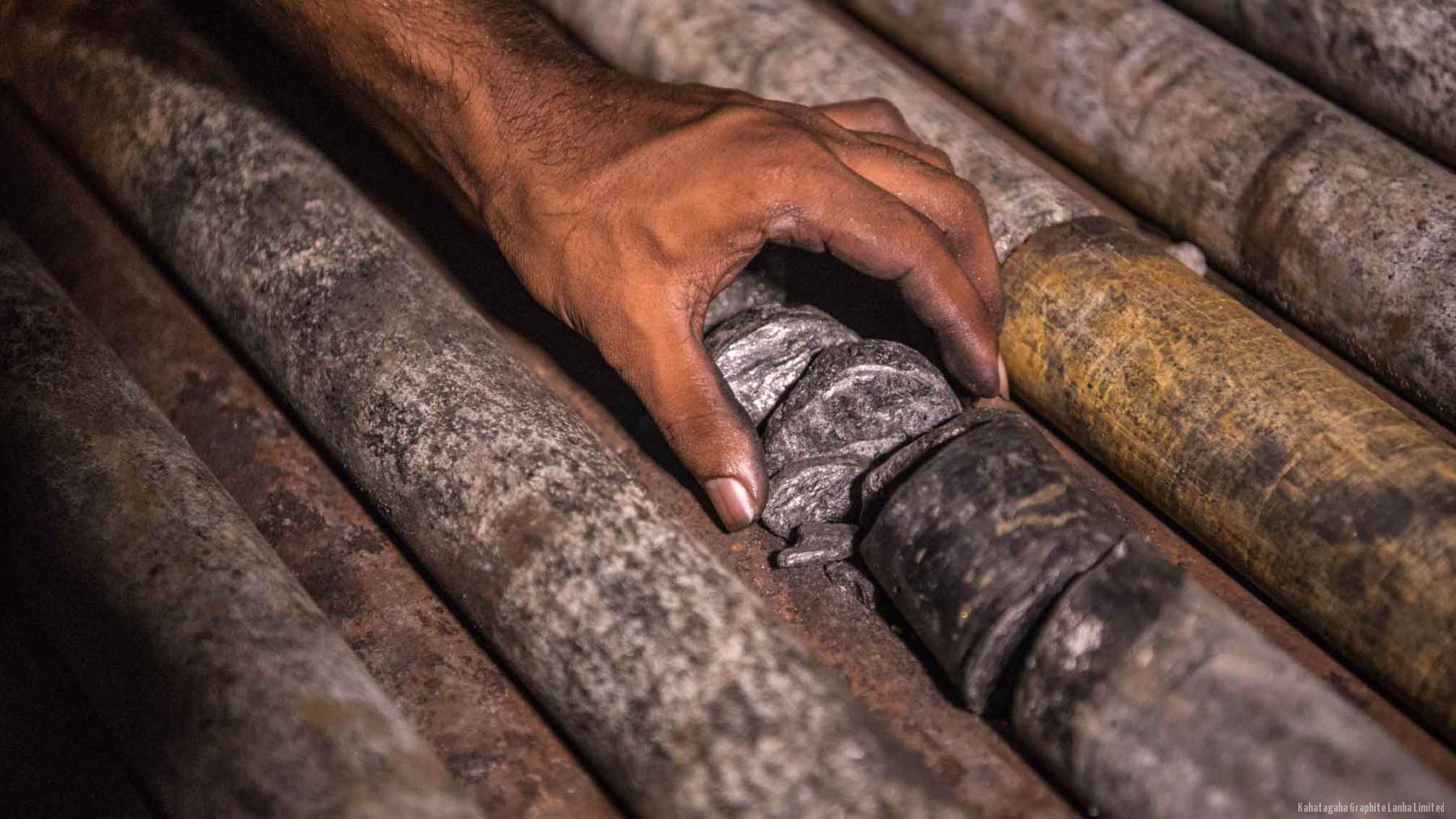 Preview of concept B: a hand resting on drill core with a band of graphite visible in the rock.